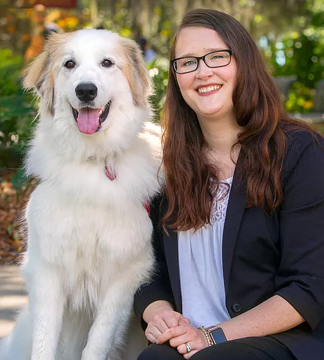 Ellen smiles into the camera, kneeling down next to her great pyrenees service dog